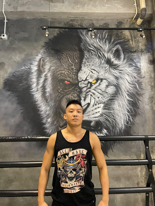 A professional fighter standing with his arms down. He is wearing the black color tank top with The Immortal Warriors design on it.