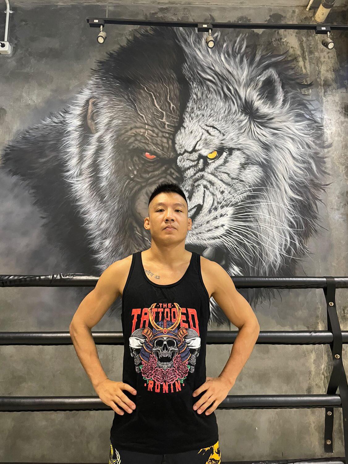 A young professional fighter standing with his hands on his hips. He is wearing a black tank top with The Tattooed Ronin design on it.