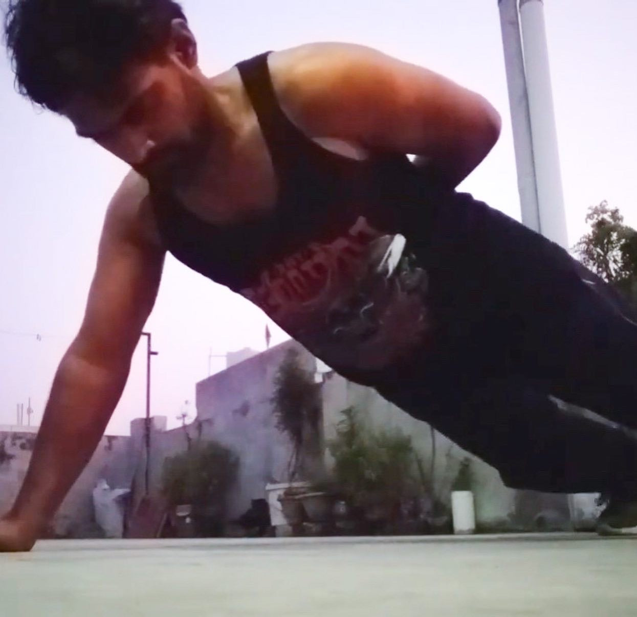 A young man doing one armed push ups while he is wearing a black tank top with The Tattooed Ronin design on it.