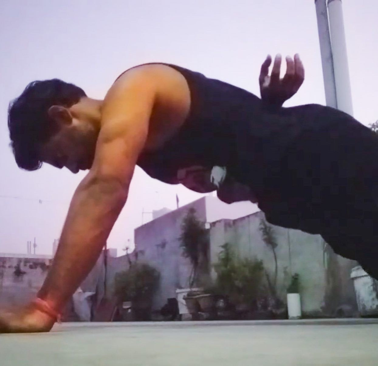 A side view of a man doing one armed push ups while he is wearing a tank top with The Tattooed Ronin design on it. 