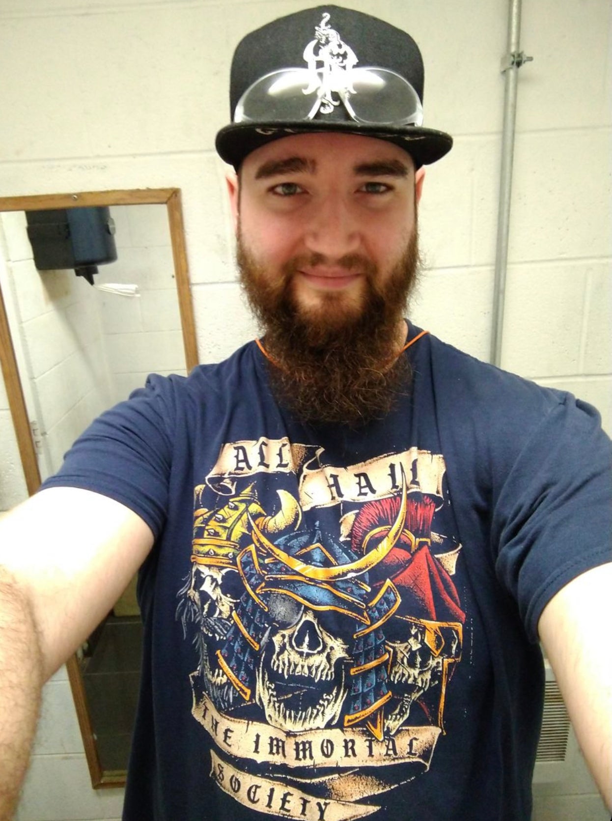 A young man taking a selfie wearing a navy color t shirt with The Immortal Warriors designs on it.  