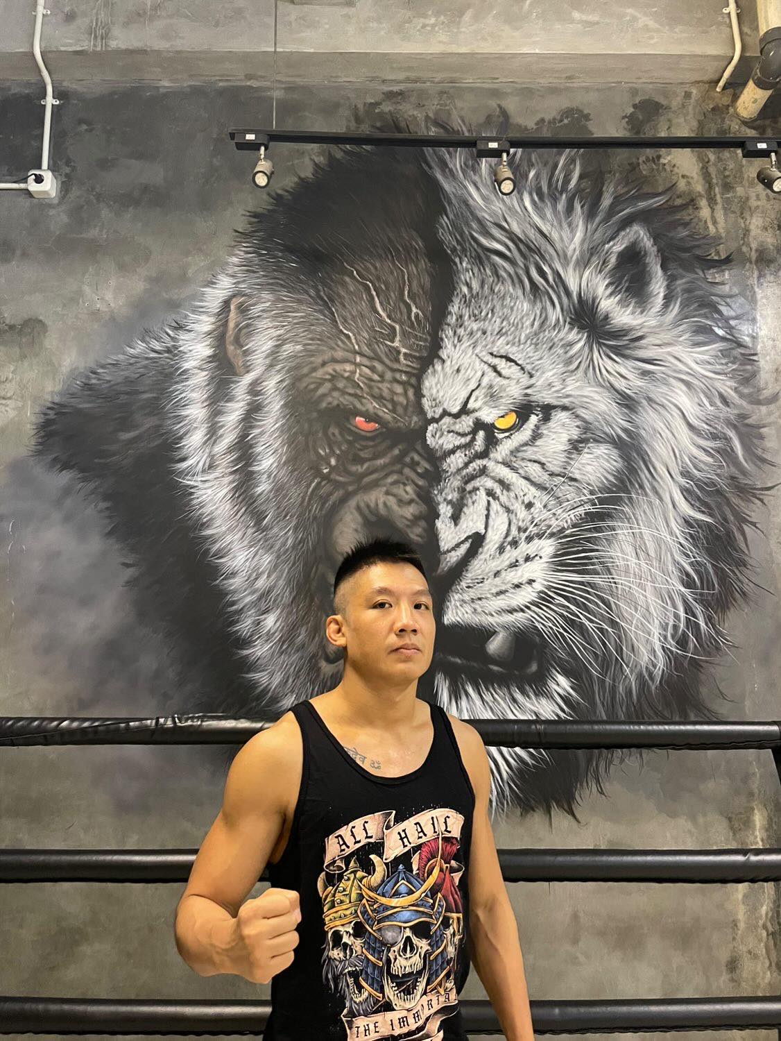 A professional fighter standing with his right fist out posing. He is wearing the black color tank top with The Immortal Warriors design on it. 