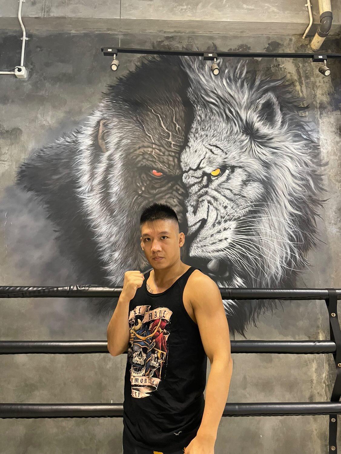 A professional fighter standing  to the side with his right fist out posing. He is wearing the black color tank top with The Immortal Warriors design on it. 