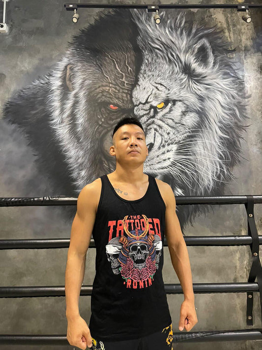 A young professional fighter standing with his chest out and shoulders back posing. He is wearing a black tank top with The Tattooed Ronin design on it. 